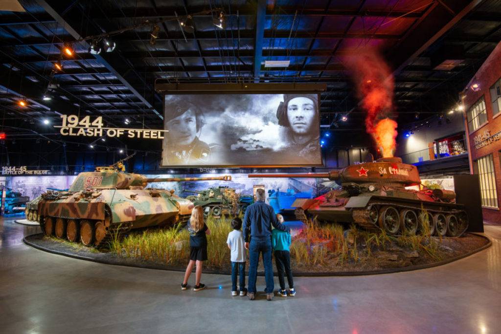 Family captivated by a film projected between two tanks. One tank has a fire effect coming out of the top