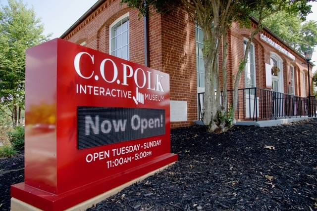 Sign outside of brick building, reading C.O. Polk Interactive Museum Open Tuesday-Sunday 11:00AM-5:00PM