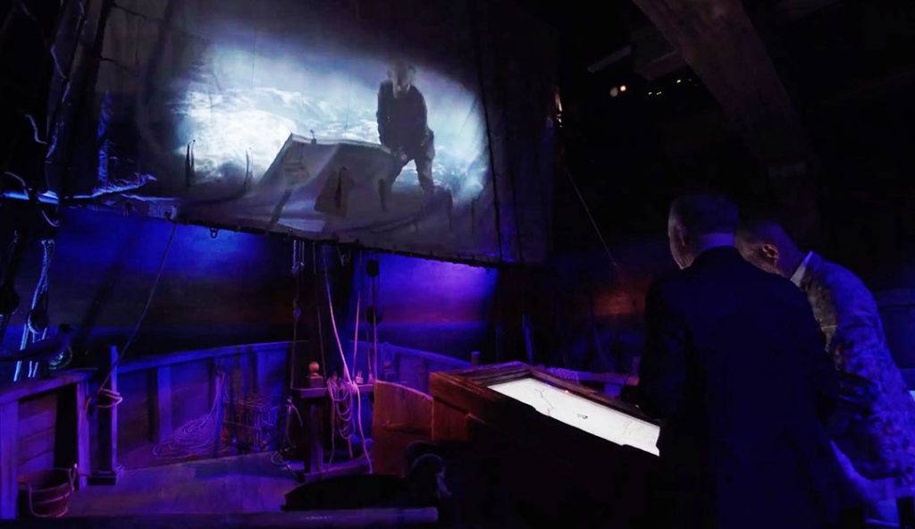 A pirate and heavy seas projected on a sail in an exhibit. Visitors chart course on a touch screen.