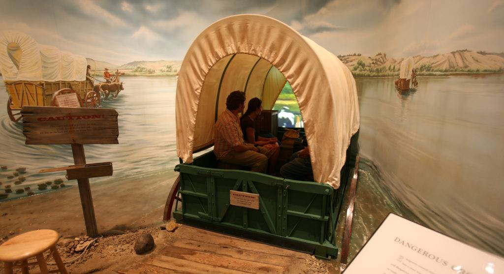 People ride in a wagon that appears to be driving into a river