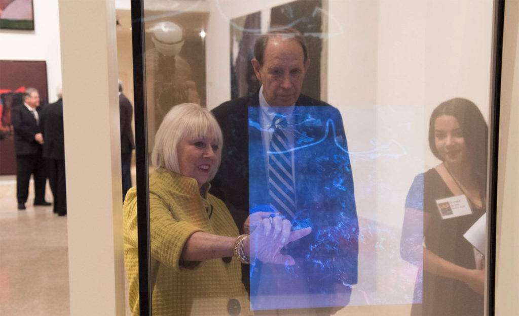 Woman interacting with a transparent touch screen in an art gallery