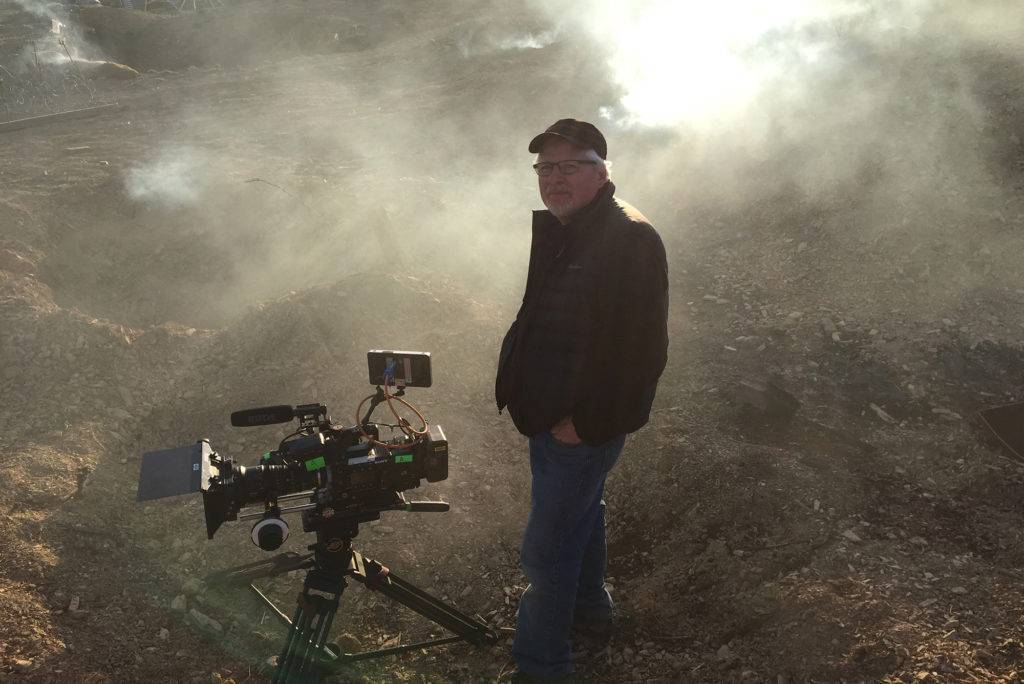 Director standing with camera in a dusty pit of dirt