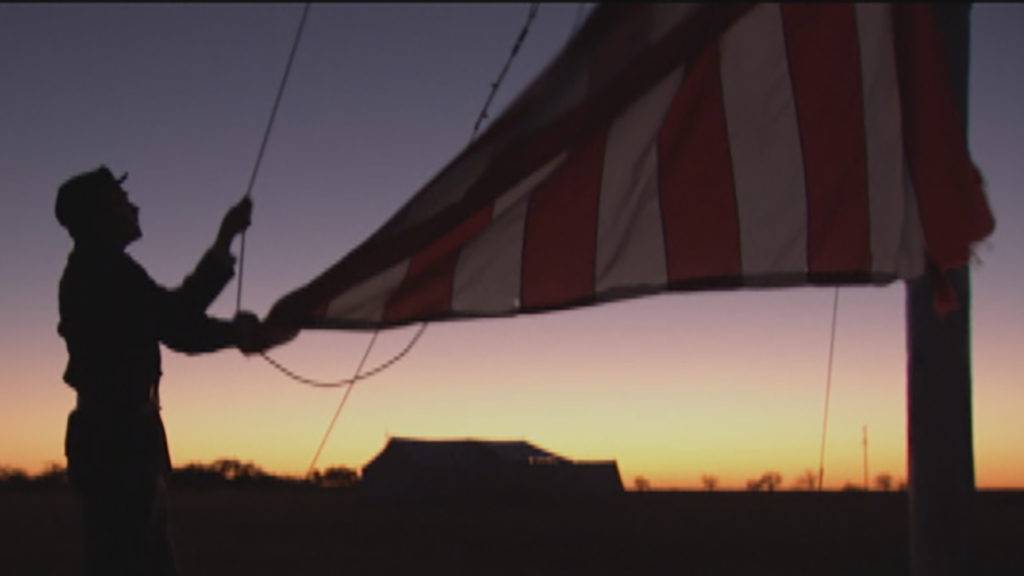 Man raising an American flag during sunrise