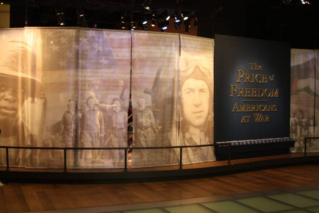Backlit tapestries of soldiers and pilots, alongside an entrance sign saying "The Price of Freedom: Americans at War"