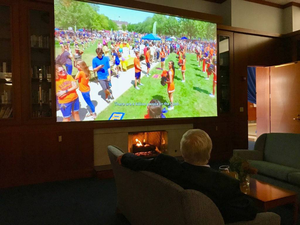 Orientation film of students gathering on the quad, shown in a cozy room over a fireplace