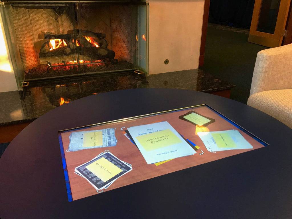 Touch-table by a cozy-fireplace, with archival documents showing the history and culture of the university